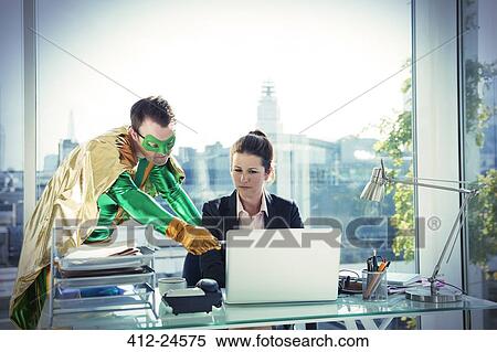 Stock Photography - Superhero helping businesswoman working at office desk. Fotosearch