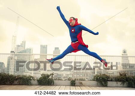 Stock Image - Superhero jumping on city rooftop. Fotosearch