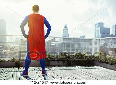 Stock Photo - Superhero looking at view from city rooftop. Fotosearch