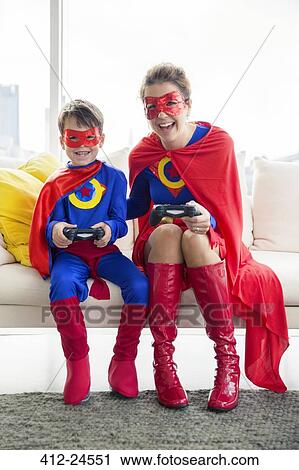 Stock Image - Superhero mother and son playing video game in living room. Fotosearch