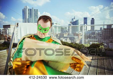 Stock Image - Superhero reading newspaper on city rooftop. Fotosearch