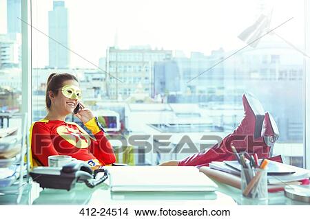 Picture - Superhero talking on cell phone at office desk. Fotosearch