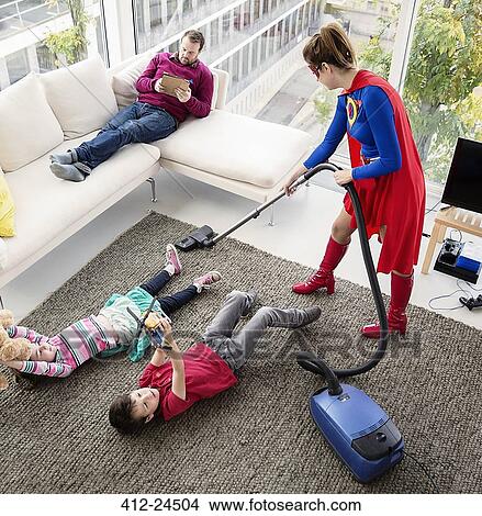Superhero vacuuming around family in living room View Large Photo Image Picture - Superhero vacuuming around family in living room. Fotosearch
