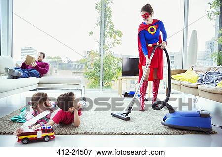 Superhero vacuuming around family in living room View Large Photo Image Stock Photo - Superhero vacuuming around family in living room. Fotosearch