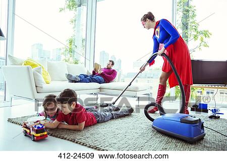 Superhero vacuuming around family in living room View Large Photo Image Stock Photo - Superhero vacuuming around family in living room. Fotosearch