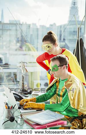 Stock Image - Superheroes working on laptop in office. Fotosearch