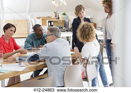 Stock Image - Group of office workers talking at desk. Fotosearch