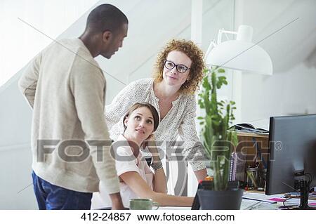 Stock Photo - Office workers talking at desk. Fotosearch