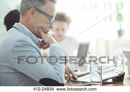 Picture - Portrait of businessman sitting at table in conference room and reading newspaper. Fotosearch