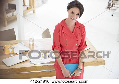 Stock Photograph - "Portrait of businesswoman wearing red dress, smiling in office". Fotosearch