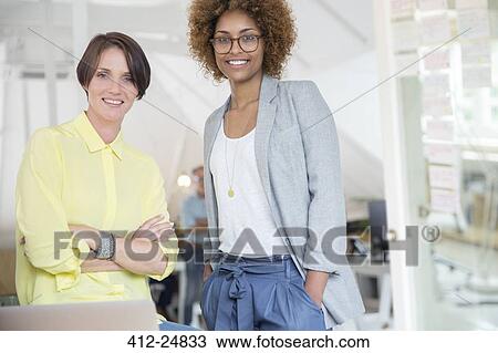 Stock Image - Portrait of female colleagues smiling in office. Fotosearch