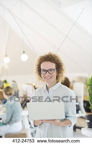Stock Image - Portrait of woman holding laptop at office. Fotosearch