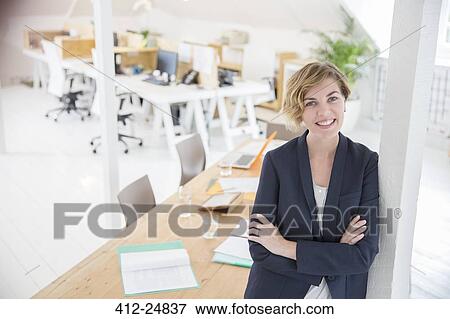 Stock Photo - Portrait of woman leaning on column in office and smiling. Fotosearch