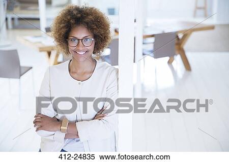 Stock Photography - Portrait of woman leaning on column in office and smiling. Fotosearch