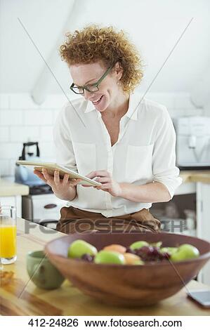"Portrait of woman sitting and looking at digital tablet in kitchen, smiling" View Large Photo Image Stock Photograph - "Portrait of woman sitting and looking at digital tablet in kitchen, smiling". Fotosearch