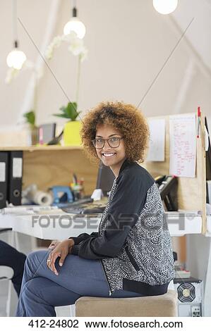 Stock Image - Portrait of woman sitting in office and smiling. Fotosearch