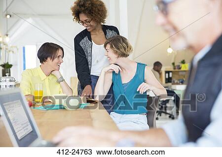 Smiling office workers talking at desk during break View Large Photo Image Stock Image - Smiling office workers talking at desk during break. Fotosearch