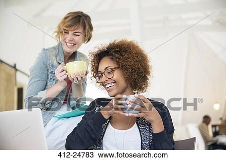 Two office workers talking at desk using laptop View Large Photo Image Stock Image - Two office workers talking at desk using laptop. Fotosearch