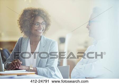 Two office workers talking at desk View Large Photo Image Stock Image - Two office workers talking at desk. Fotosearch