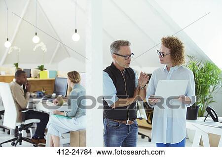 Two smiling office workers using laptop View Large Photo Image Picture - Two smiling office workers using laptop. Fotosearch