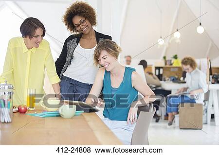Women looking at digital tablet and smiling in office View Large Photo Image Stock Photo - Women looking at digital tablet and smiling in office. Fotosearch