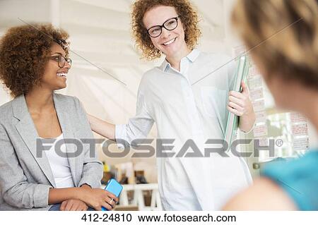 "Women smiling and talking in office, holding smart phone and laptop" View Large Photo Image Stock Image - "Women smiling and talking in office, holding smart phone and laptop". Fotosearch
