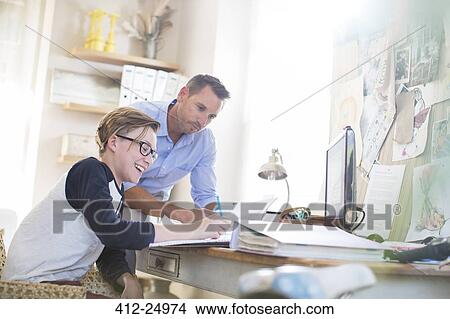Picture - Father helping teenage son doing his homework in room. Fotosearch