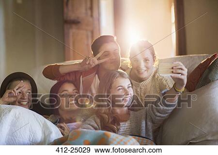 Stock Photo - Group of smiling teenagers taking selfie on sofa in living room. Fotosearch
