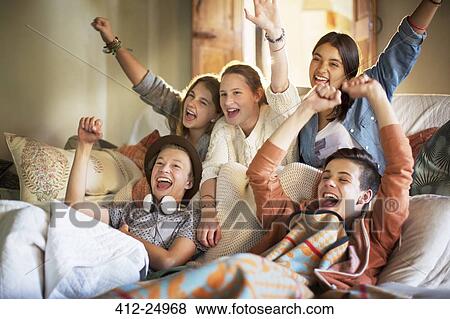 Stock Photo - Group of teenagers having fun while watching tv on sofa. Fotosearch