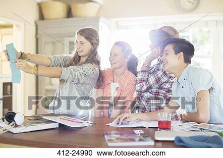 Stock Image - Group of teenagers taking selfie in dining room. Fotosearch