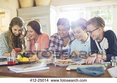 Group of teenagers using electronic devices at table in dining room View Large Photo Image Picture - Group of teenagers using electronic devices at table in dining room. Fotosearch