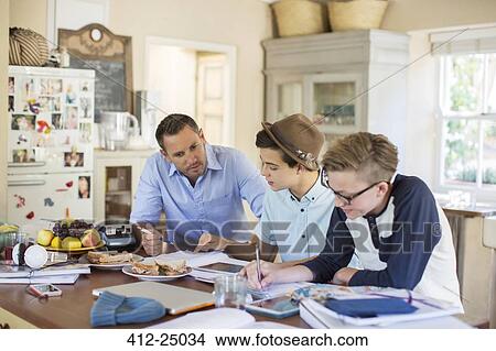 Mid adult man helping teenage boys with their homework at table View Large Photo Image Picture - Mid adult man helping teenage boys with their homework at table. Fotosearch
