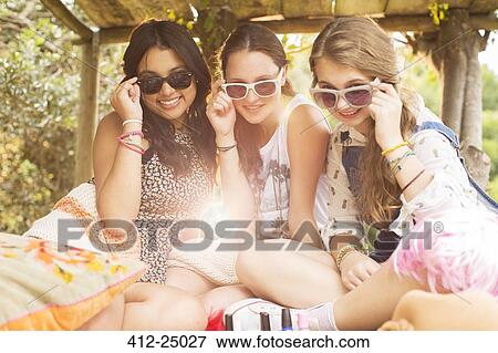 Stock Photo - Portrait of three teenage girls wearing sunglasses and sitting in tree house. Fotosearch