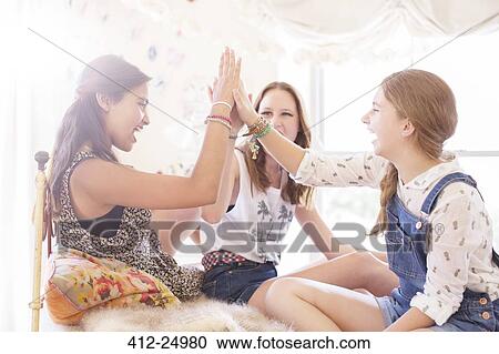 Stock Image - Three teenage girls doing high five on bed. Fotosearch