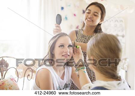 Stock Image - Three teenage girls doing make-up and brushing hair in bedroom. Fotosearch