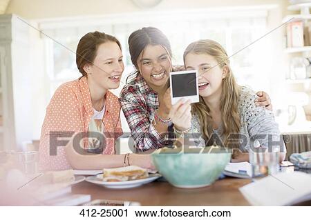 Three teenage girls looking at photograph while sitting at table View Large Photo Image Stock Image - Three teenage girls looking at photograph while sitting at table. Fotosearch