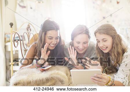 Three teenage girls lying on bed and communicating using digital tablet View Large Photo Image Stock Photograph - Three teenage girls lying on bed and communicating using digital tablet. Fotosearch