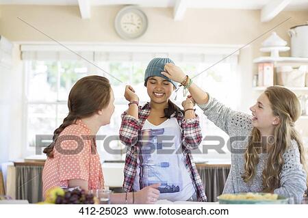 Stock Image - Three teenage girls playing with beanie in dining room. Fotosearch