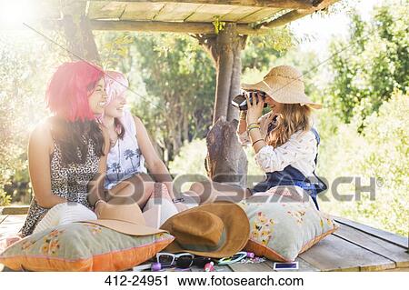 Stock Image - Three teenage girls taking photos in tree house in sunlight. Fotosearch