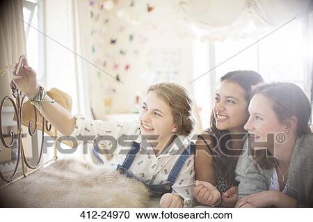 Three Teenage Girls Taking Selfie On Bed In Bedroom Stock