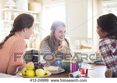 Stock Photo - Three teenage girls talking at table in dining room. Fotosearch