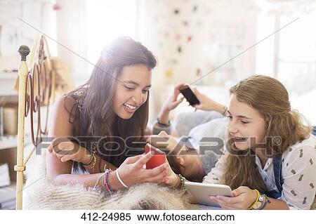 Stock Photography - Three teenage girls using electronic devices while lying on bed. Fotosearch
