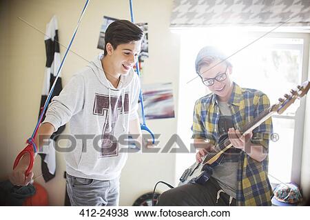 Two teenage boys having fun and playing electric guitar in room View Large Photo Image Stock Photo - Two teenage boys having fun and playing electric guitar in room. Fotosearch