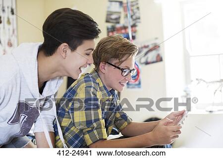 Stock Image - Two teenage boys having fun while using digital tablet in room. Fotosearch