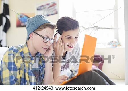 Stock Photo - Two teenage boys sharing laptop and headphones in room. Fotosearch