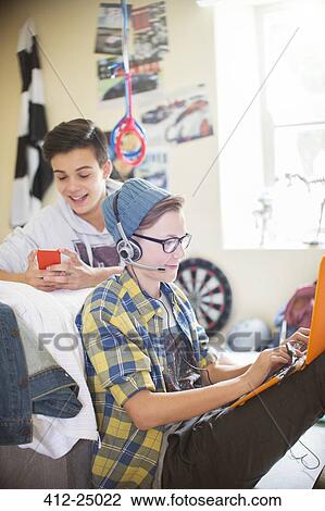 Two teenage boys using electronic devices in room View Large Photo Image Stock Image - Two teenage boys using electronic devices in room. Fotosearch