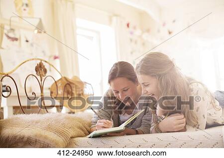 Two teenage girls lying on bed and writing in notebook View Large Photo Image Stock Image - Two teenage girls lying on bed and writing in notebook. Fotosearch