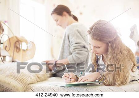 Stock Image - Two teenage girls on bed writting in notepads. Fotosearch