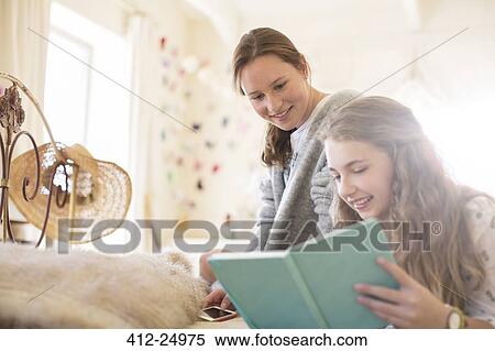 Stock Photography - Two teenage girls reading book together on bed. Fotosearch
