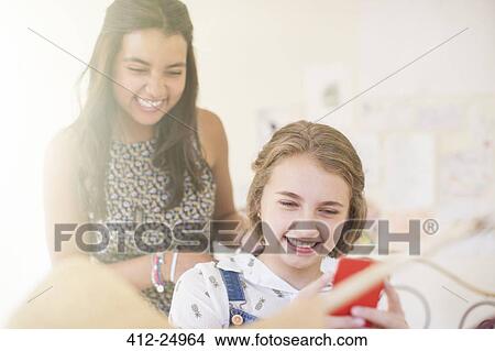 Picture - Two teenage girls sharing smartphone and smiling. Fotosearch